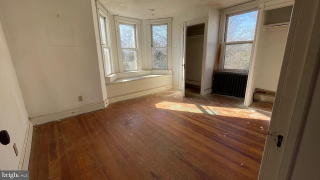 unfurnished bedroom featuring hardwood / wood-style flooring, radiator, baseboards, and multiple closets