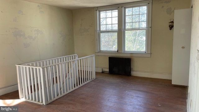 empty room with radiator heating unit, baseboards, and hardwood / wood-style flooring