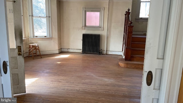 unfurnished room with stairway, a healthy amount of sunlight, radiator, and wood-type flooring