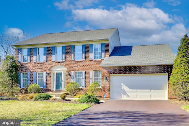 colonial-style house featuring roof with shingles, a front lawn, a garage, aphalt driveway, and brick siding