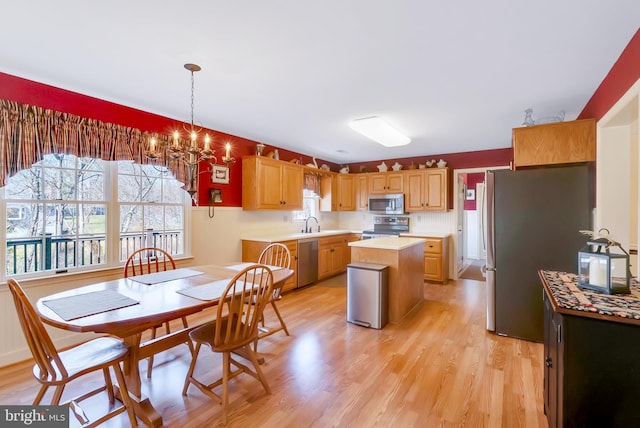 kitchen with light wood-type flooring, a sink, a center island, stainless steel appliances, and light countertops