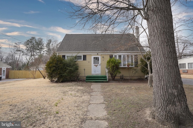 cape cod house with entry steps, a chimney, roof with shingles, and fence