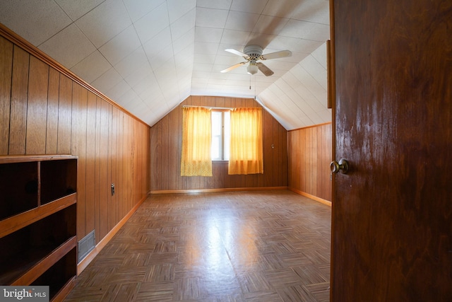 additional living space featuring visible vents, lofted ceiling, a ceiling fan, wooden walls, and baseboards