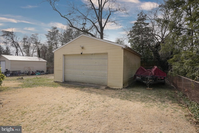 detached garage featuring dirt driveway and fence