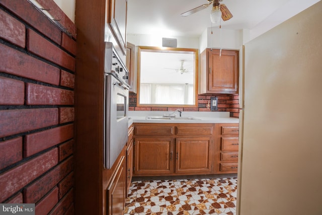 kitchen with a ceiling fan, brown cabinetry, light floors, a sink, and light countertops