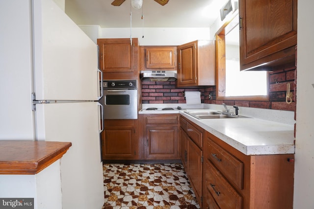 kitchen with white appliances, ceiling fan, a sink, under cabinet range hood, and brown cabinets