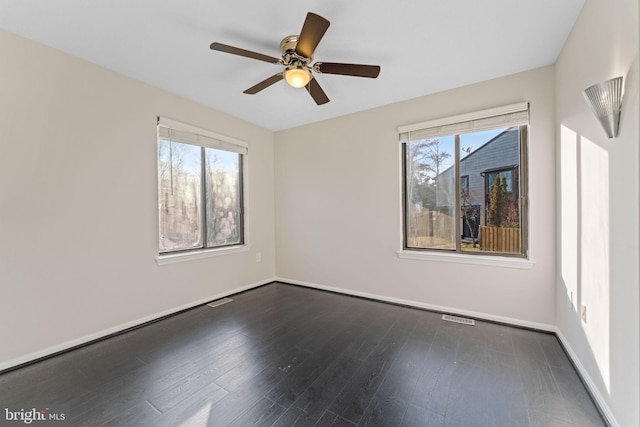 empty room featuring dark wood-style floors, plenty of natural light, baseboards, and visible vents