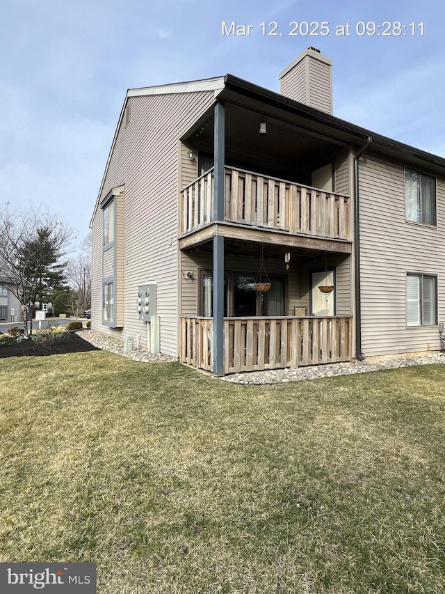 rear view of property with a balcony, a yard, and a chimney