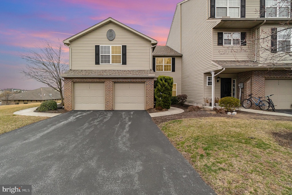 traditional-style home with aphalt driveway, brick siding, a garage, and a yard