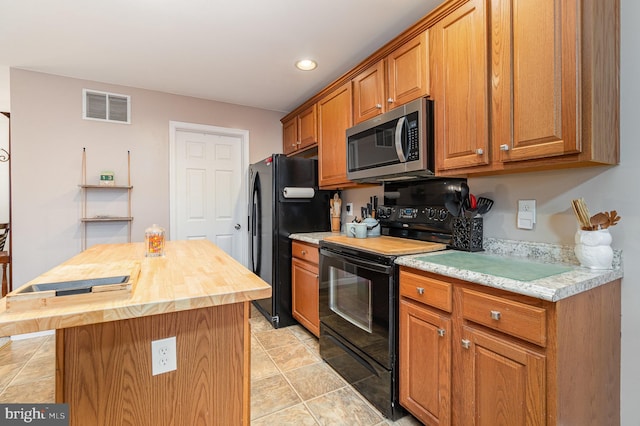 kitchen featuring visible vents, a center island, butcher block counters, brown cabinets, and black appliances