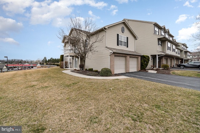 view of side of home with brick siding, a yard, an attached garage, and driveway