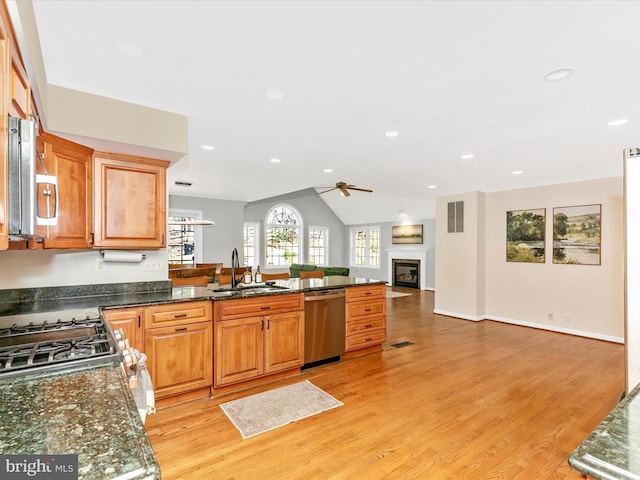 kitchen with a sink, stainless steel dishwasher, open floor plan, a glass covered fireplace, and a peninsula