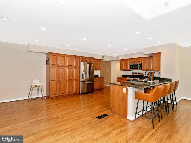 kitchen featuring light wood finished floors, a peninsula, brown cabinetry, stainless steel appliances, and a sink