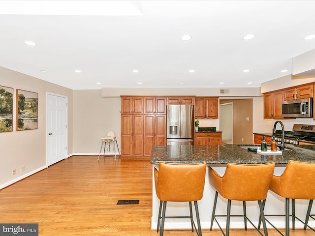 kitchen with a breakfast bar area, recessed lighting, light wood-style flooring, brown cabinetry, and stainless steel appliances