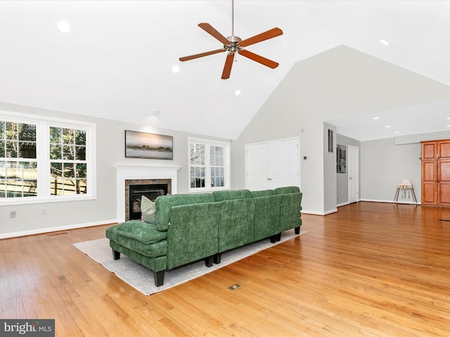 living area with baseboards, high vaulted ceiling, recessed lighting, a brick fireplace, and light wood-type flooring