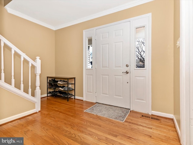 foyer with visible vents, crown molding, baseboards, stairway, and wood finished floors