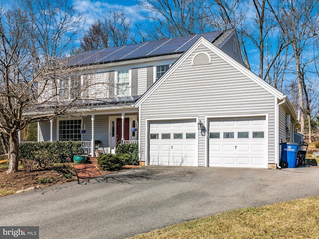 traditional home featuring roof mounted solar panels, a porch, an attached garage, and driveway