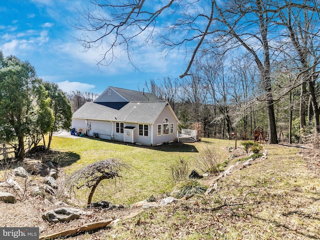 view of home's exterior with a lawn, a deck, and roof with shingles