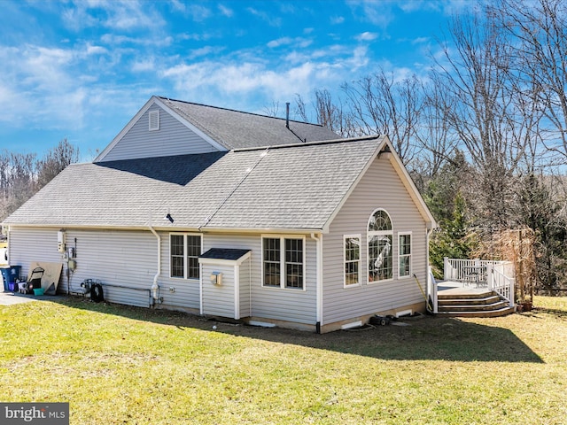 back of property with a wooden deck, a yard, and roof with shingles