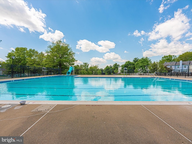 community pool with a patio area, fence, and a water slide