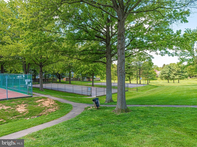 view of property's community with a tennis court, a lawn, and fence