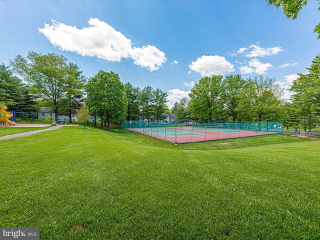 view of tennis court featuring fence, a lawn, and playground community