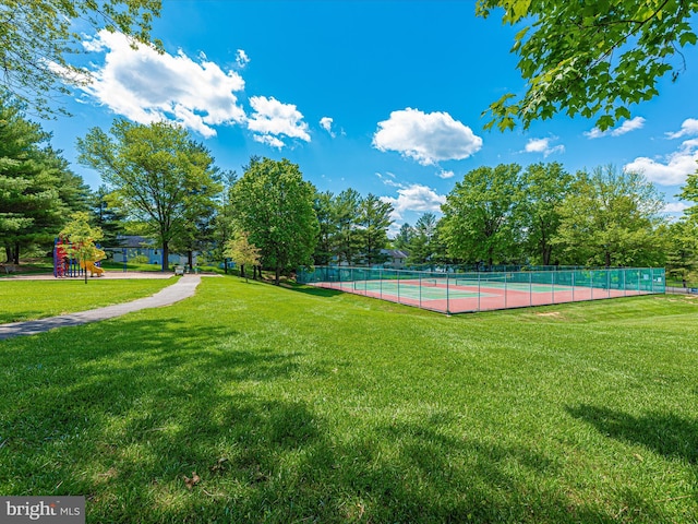 view of tennis court with playground community, a yard, and fence