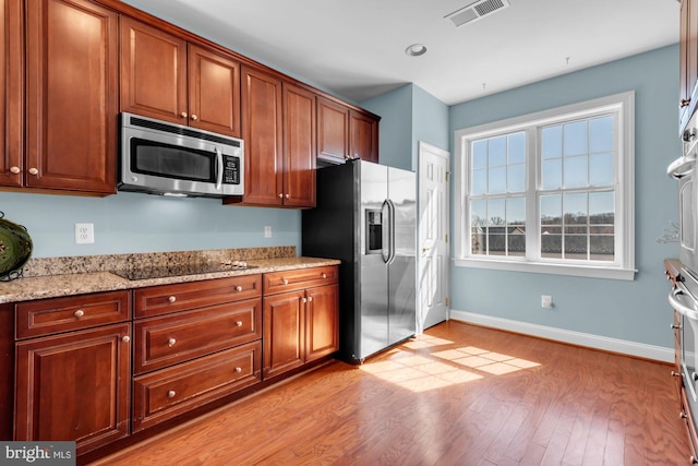 kitchen featuring visible vents, baseboards, light stone countertops, light wood-style flooring, and stainless steel appliances