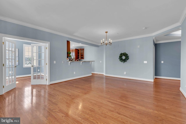 unfurnished living room with an inviting chandelier, wood finished floors, baseboards, and ornamental molding