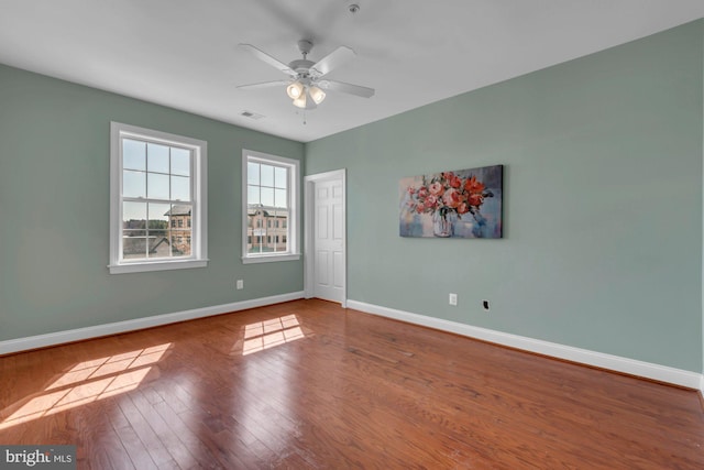 empty room with visible vents, a ceiling fan, baseboards, and hardwood / wood-style floors