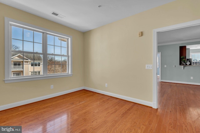 empty room with visible vents, wood finished floors, baseboards, and ornamental molding