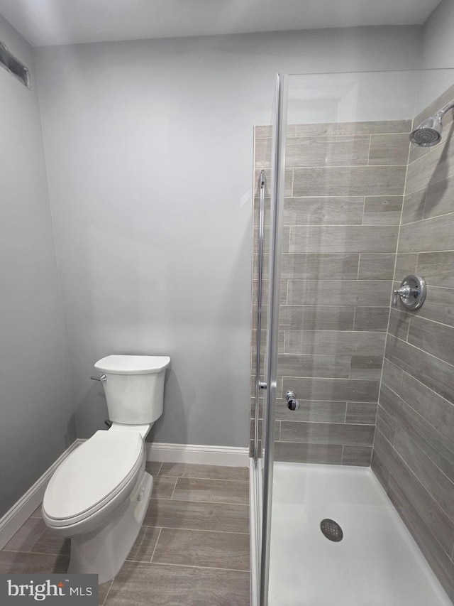 bathroom featuring baseboards, toilet, and a stall shower