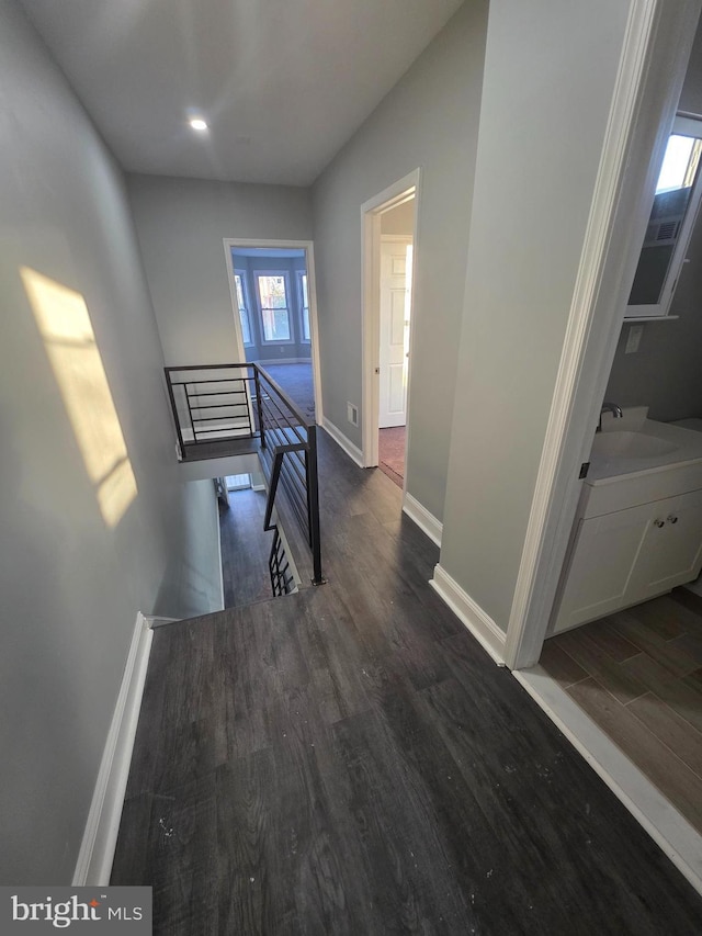 corridor with an upstairs landing, a sink, baseboards, and wood finished floors