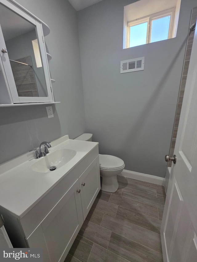 full bathroom featuring wood finish floors, visible vents, toilet, baseboards, and vanity