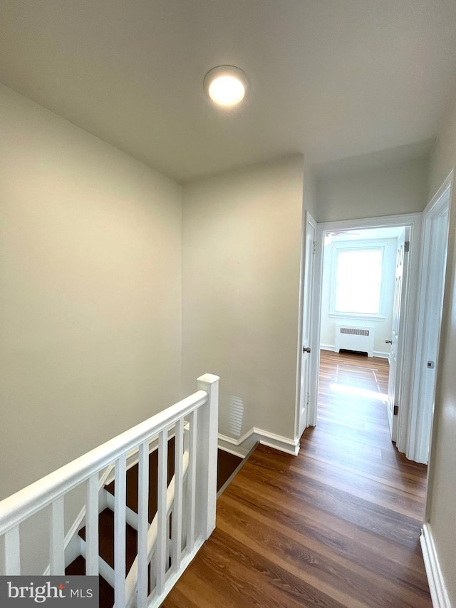 corridor featuring dark wood-type flooring, radiator heating unit, an upstairs landing, and baseboards