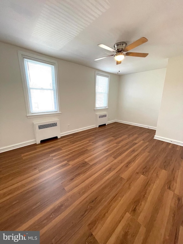 empty room featuring radiator heating unit, wood finished floors, and baseboards