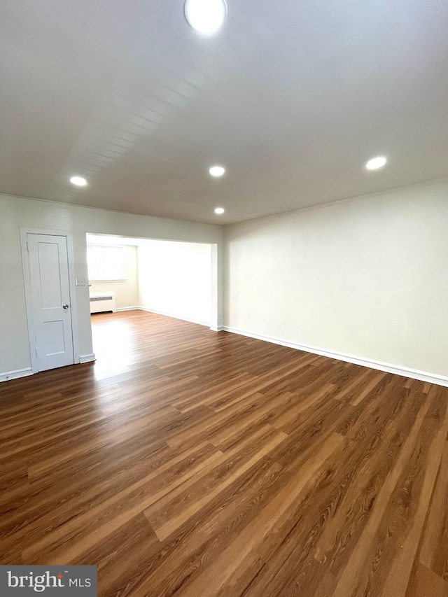 below grade area with dark wood finished floors, recessed lighting, a baseboard heating unit, and baseboards