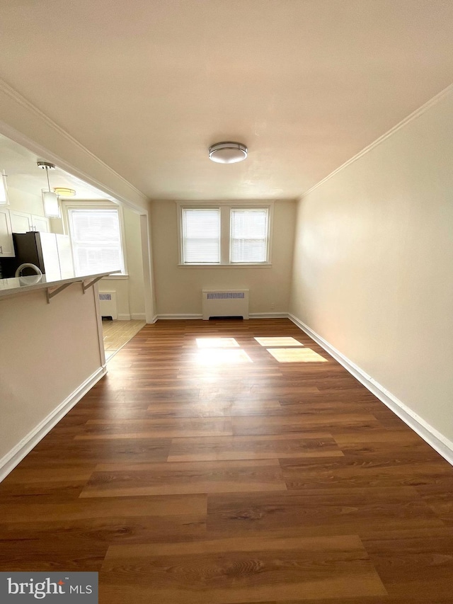 unfurnished room featuring radiator heating unit, wood finished floors, baseboards, and ornamental molding