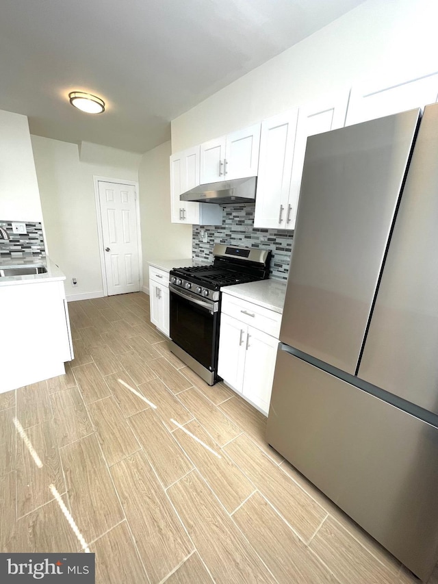 kitchen with a sink, white cabinets, under cabinet range hood, appliances with stainless steel finishes, and tasteful backsplash