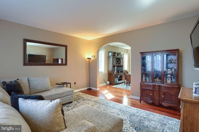 living area featuring arched walkways, baseboards, and wood finished floors