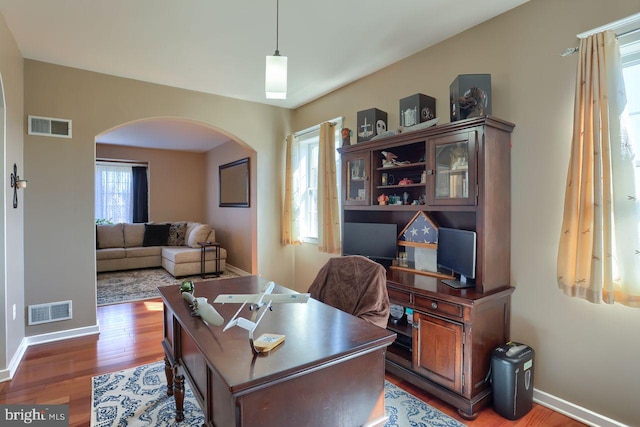 office area featuring visible vents, wood finished floors, arched walkways, and baseboards