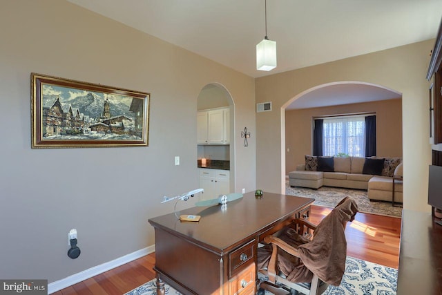 home office featuring visible vents, baseboards, arched walkways, and wood finished floors