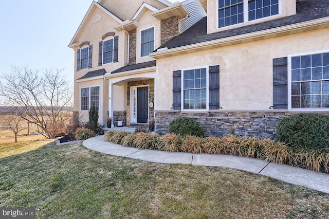 view of front of home featuring stucco siding, stone siding, roof with shingles, and a front yard