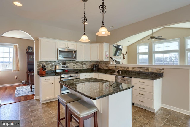 kitchen featuring decorative backsplash, appliances with stainless steel finishes, a peninsula, white cabinets, and a sink