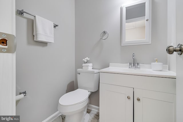 half bathroom with vanity, toilet, baseboards, and marble finish floor