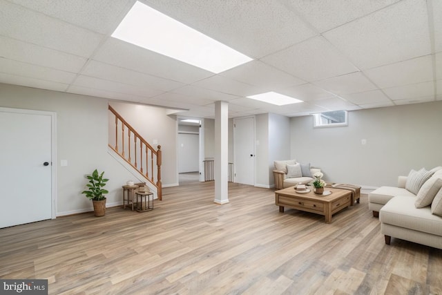 living area featuring light wood finished floors, stairway, baseboards, and a drop ceiling