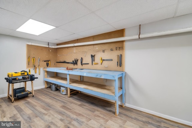 interior space with baseboards, a paneled ceiling, a workshop area, and wood finished floors