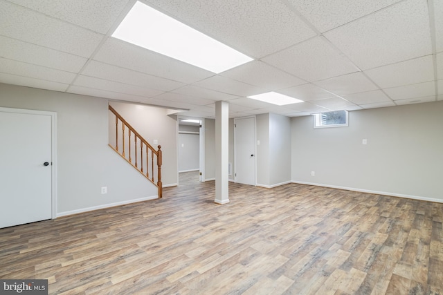 below grade area featuring stairs, wood finished floors, baseboards, and a paneled ceiling