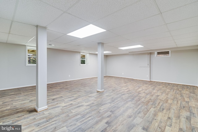 basement with a drop ceiling, plenty of natural light, baseboards, and wood finished floors