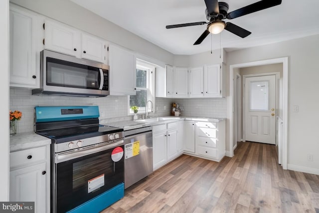 kitchen featuring light wood-style flooring, a sink, light countertops, appliances with stainless steel finishes, and white cabinetry